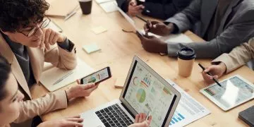 Several people around a table working together and using smartphones and laptops.