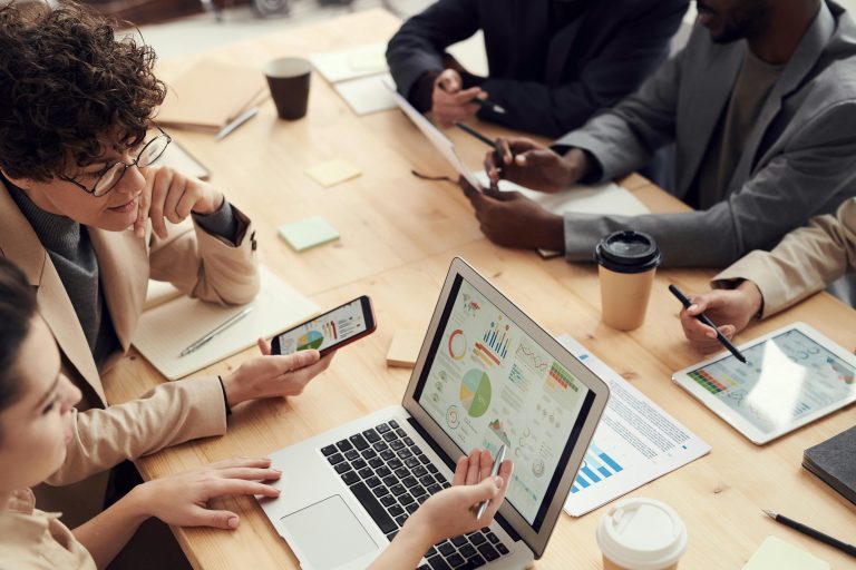 Several people around a table working together and using smartphones and laptops.